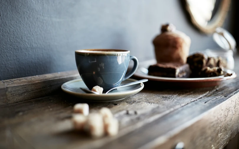 there is a cup on the wooden table and a plate with sweets