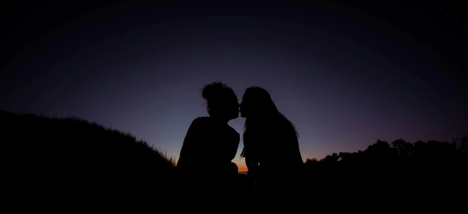 two people sitting in the grass at sunset