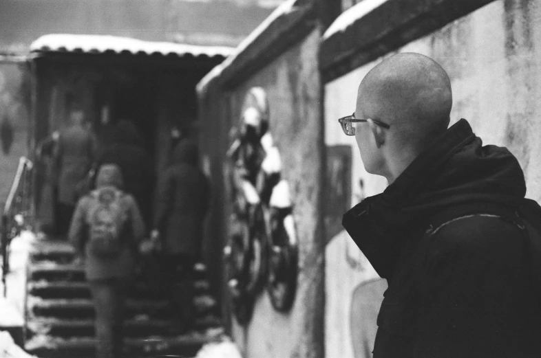 a bald headed man walking through the snow next to a building