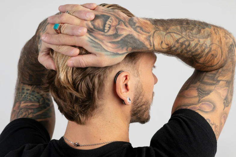 a man is putting his hands in the hair with tattoos on both arms