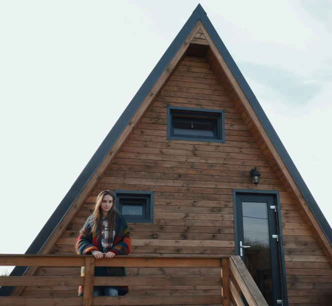 a beautiful young lady standing outside of a large wooden cabin