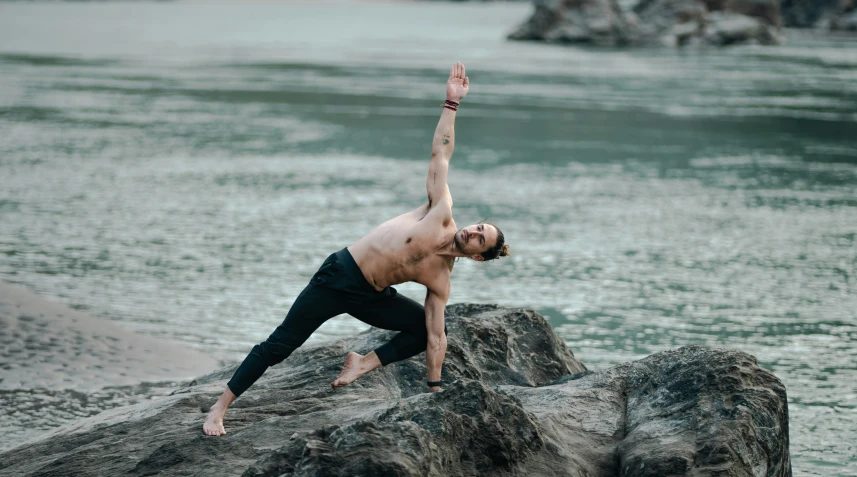 a man is doing yoga exercises on a rock by the water