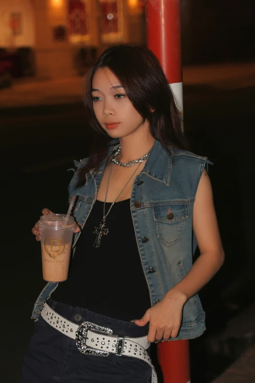 a young woman holds a drink next to a street pole