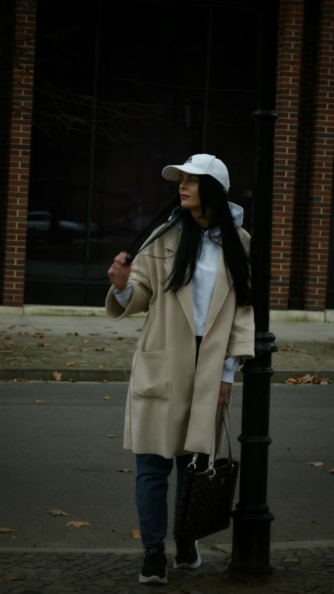 a lady is standing on the street holding onto a light post