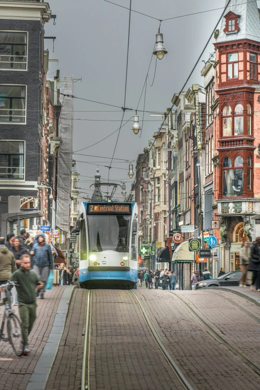 a tram in a city, running down a street, with pedestrians