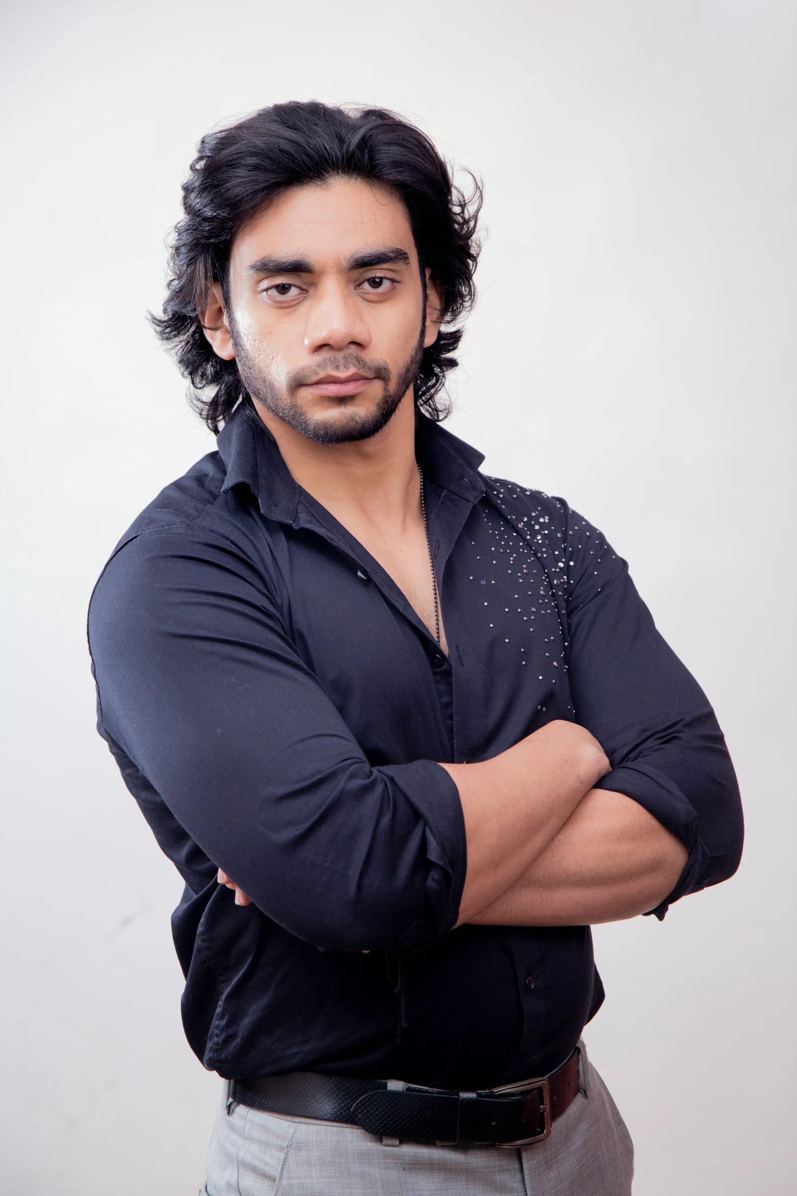 man standing up in front of white background with his arms folded