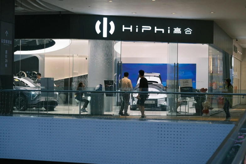 a car showroom with people looking at vehicles in the reflection