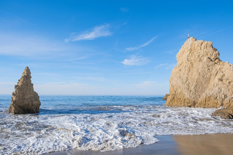 a wave rolls in near the sand and rocks on the beach