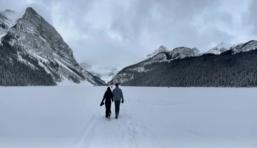 two people are walking in the snow toward a mountain