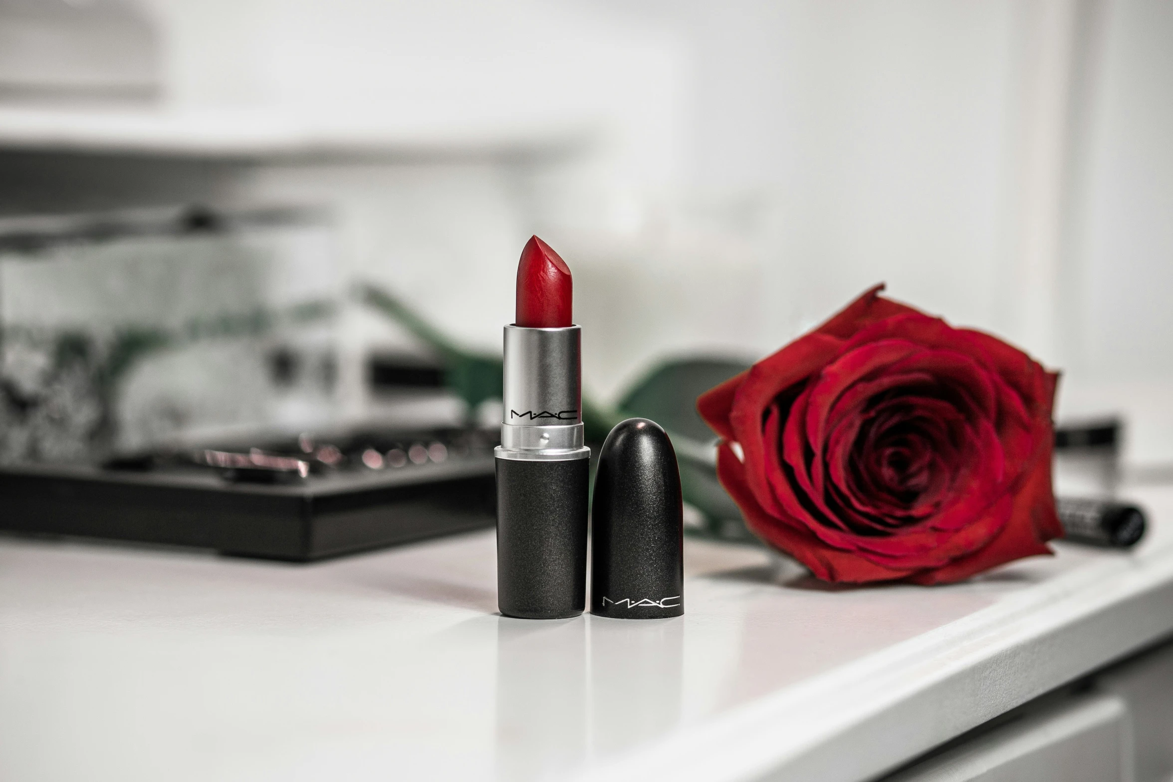 lipstick on a table next to a rose