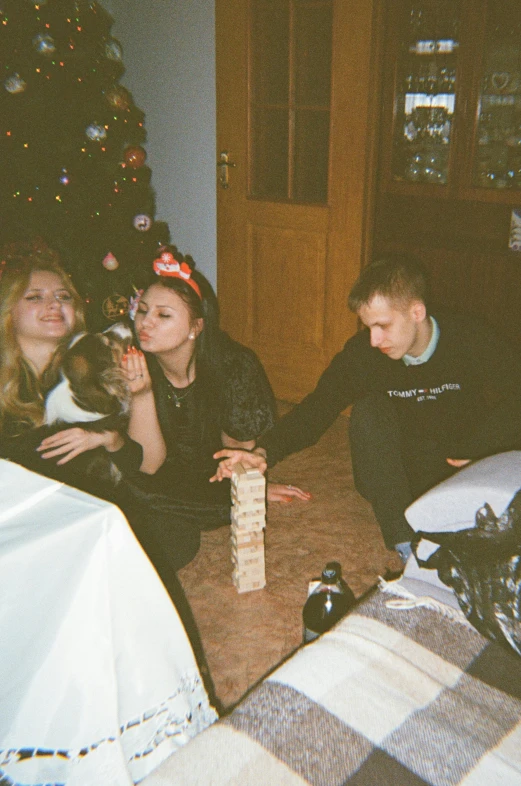 two couples posing for a picture, sitting near a christmas tree