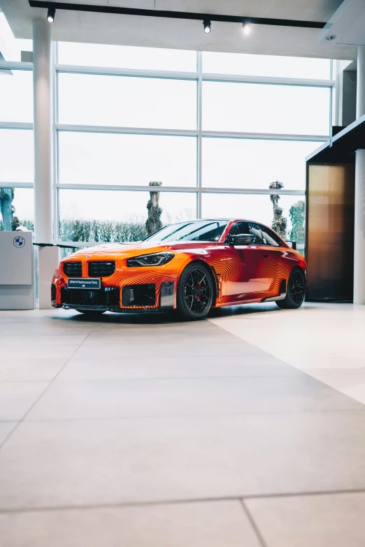 an orange car is in a showroom with a large glass wall