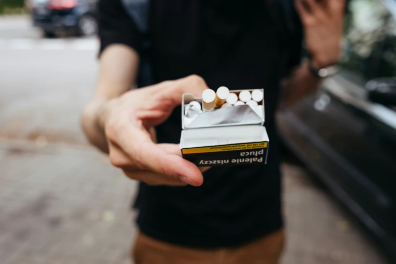 a person holding a cigarette and a small pack of cigarettes