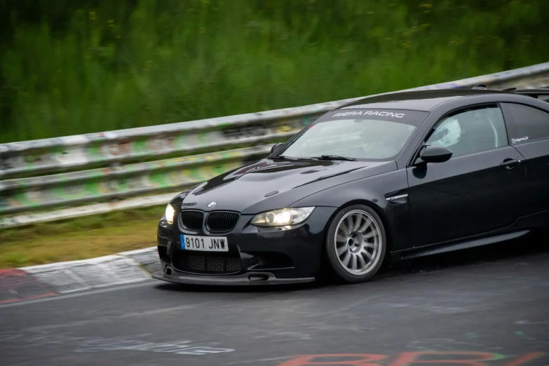 a black car driving down a track next to tall grass