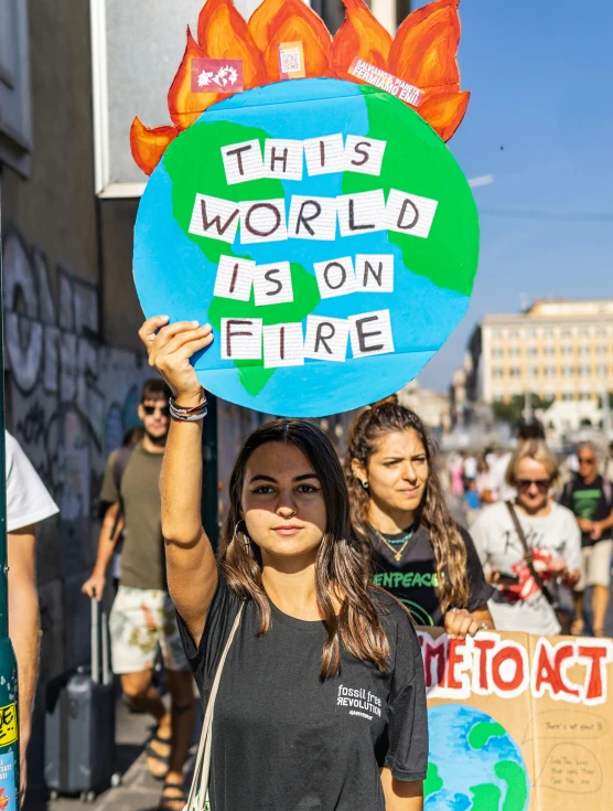 a woman holding up a blue sign reading, this world is on fire