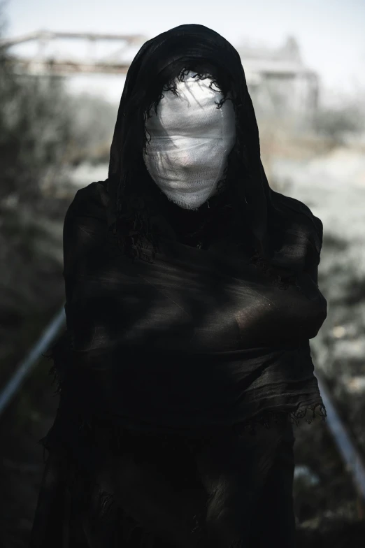 a ghostly woman in a black dress standing near train tracks