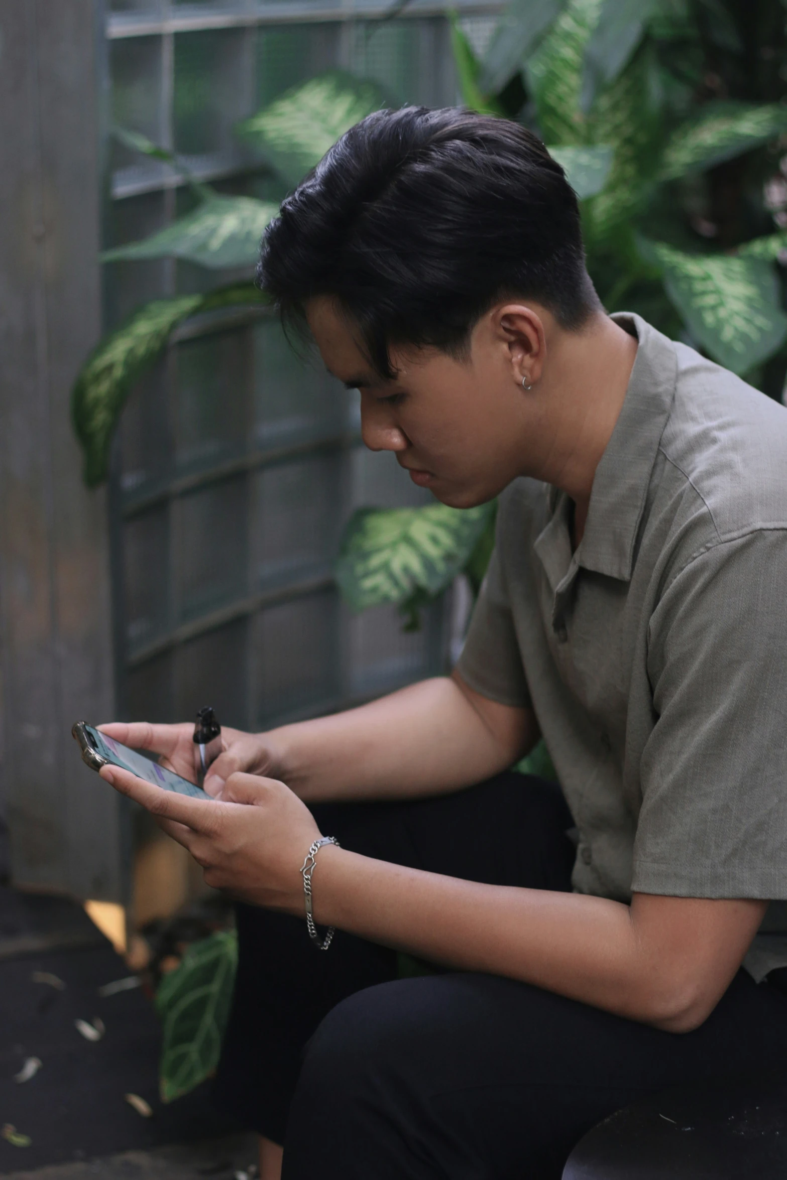 a young man sitting in front of a plant looking at a cell phone