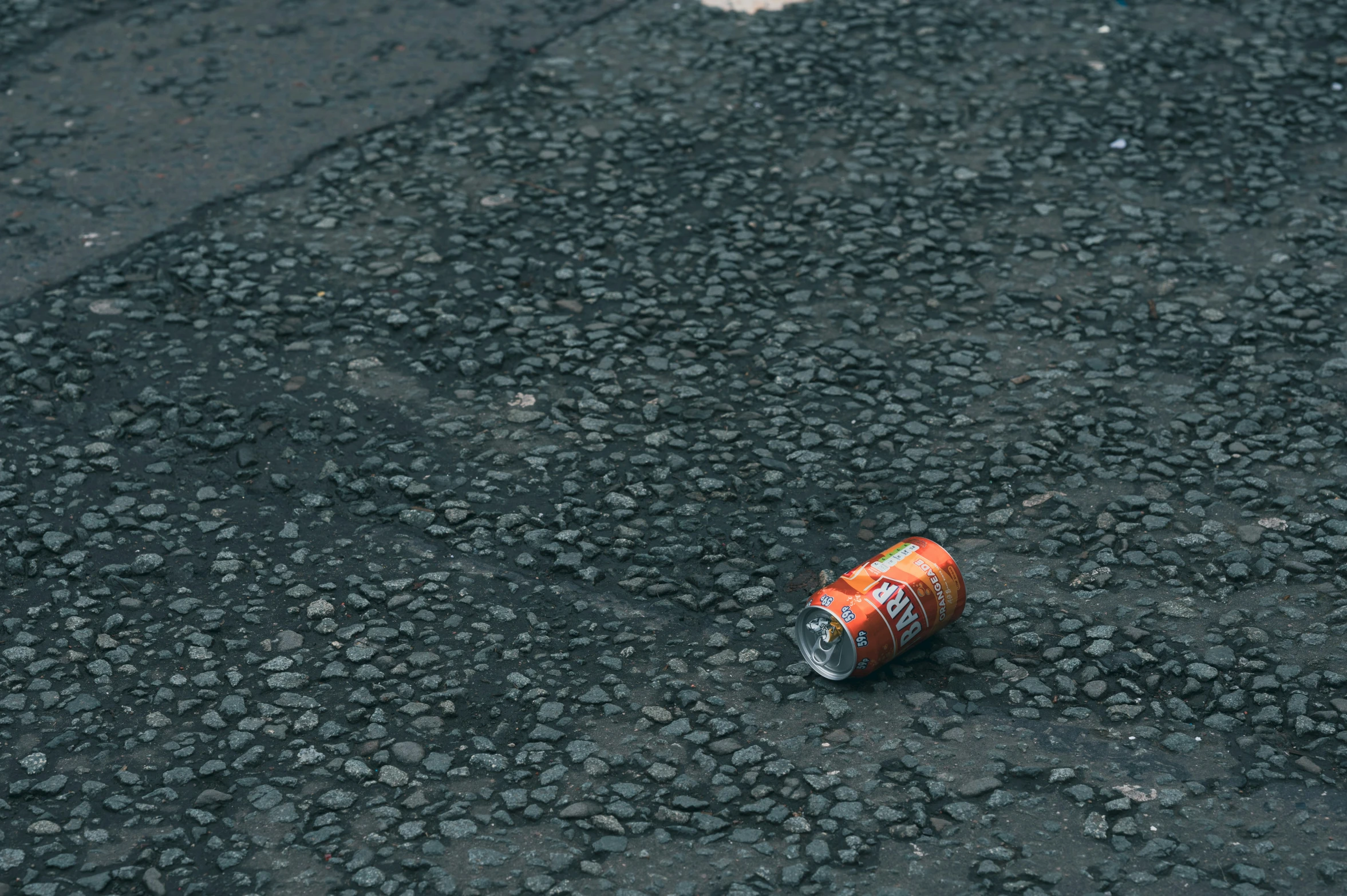 a can of soda sitting on the ground with a sidewalk below