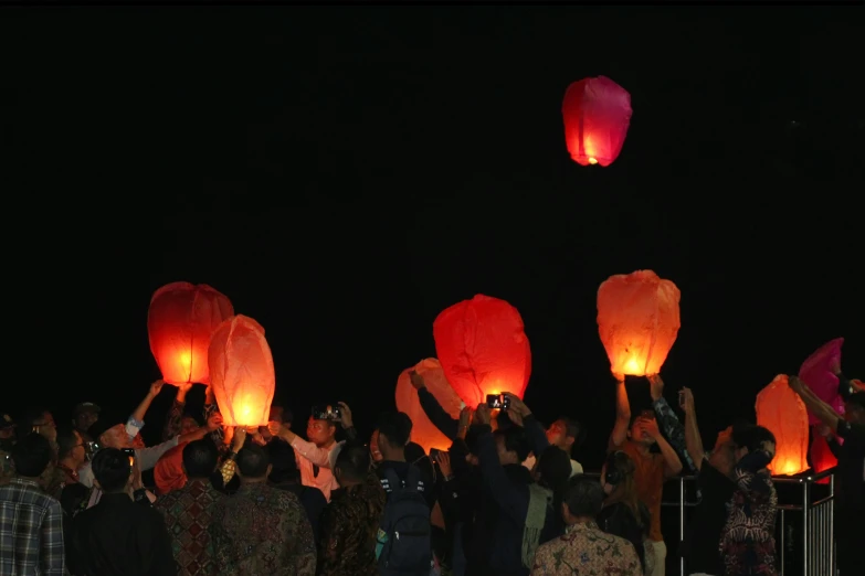 several people holding up bright chinese lanterns at night