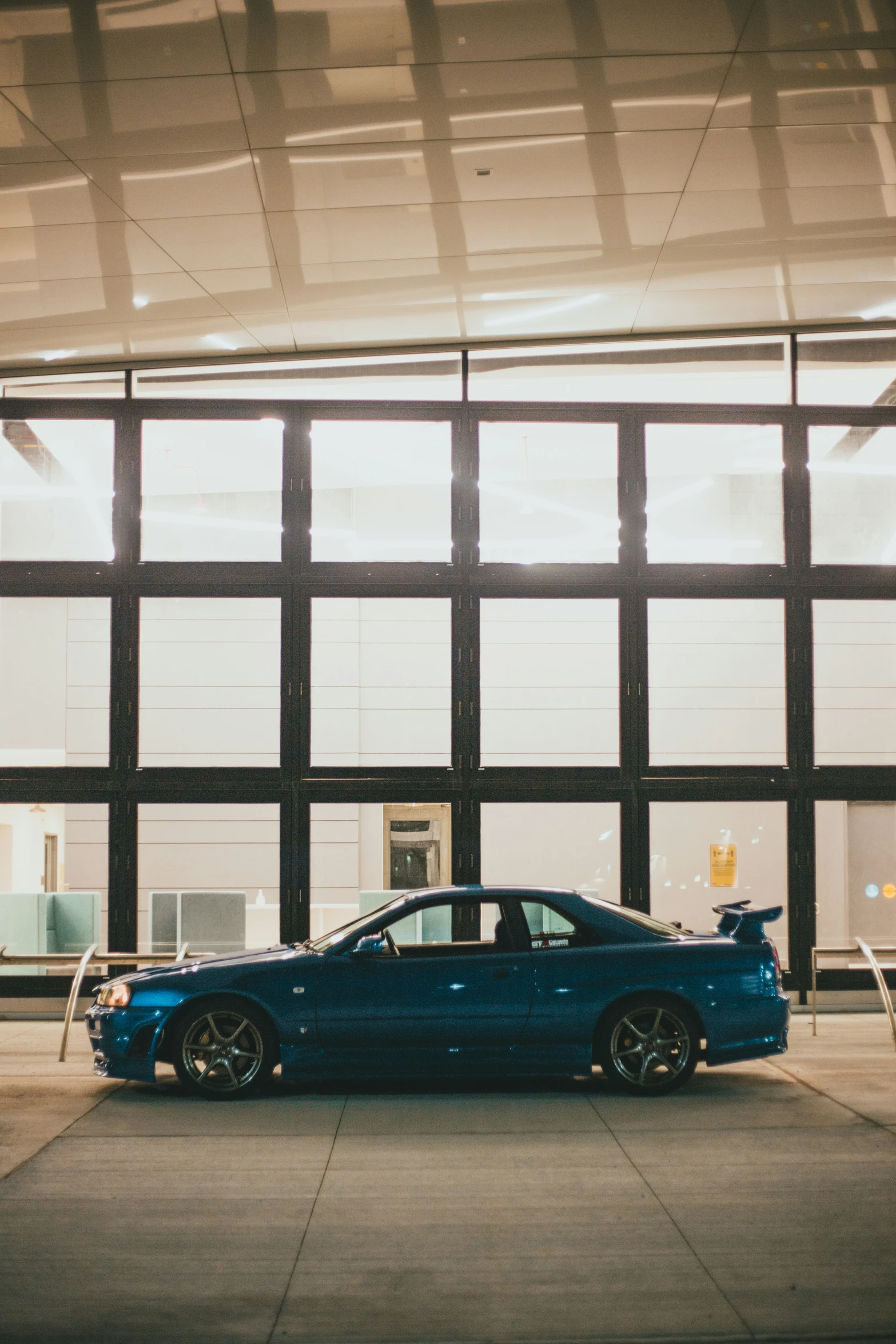 a blue car parked near large windows in a parking lot