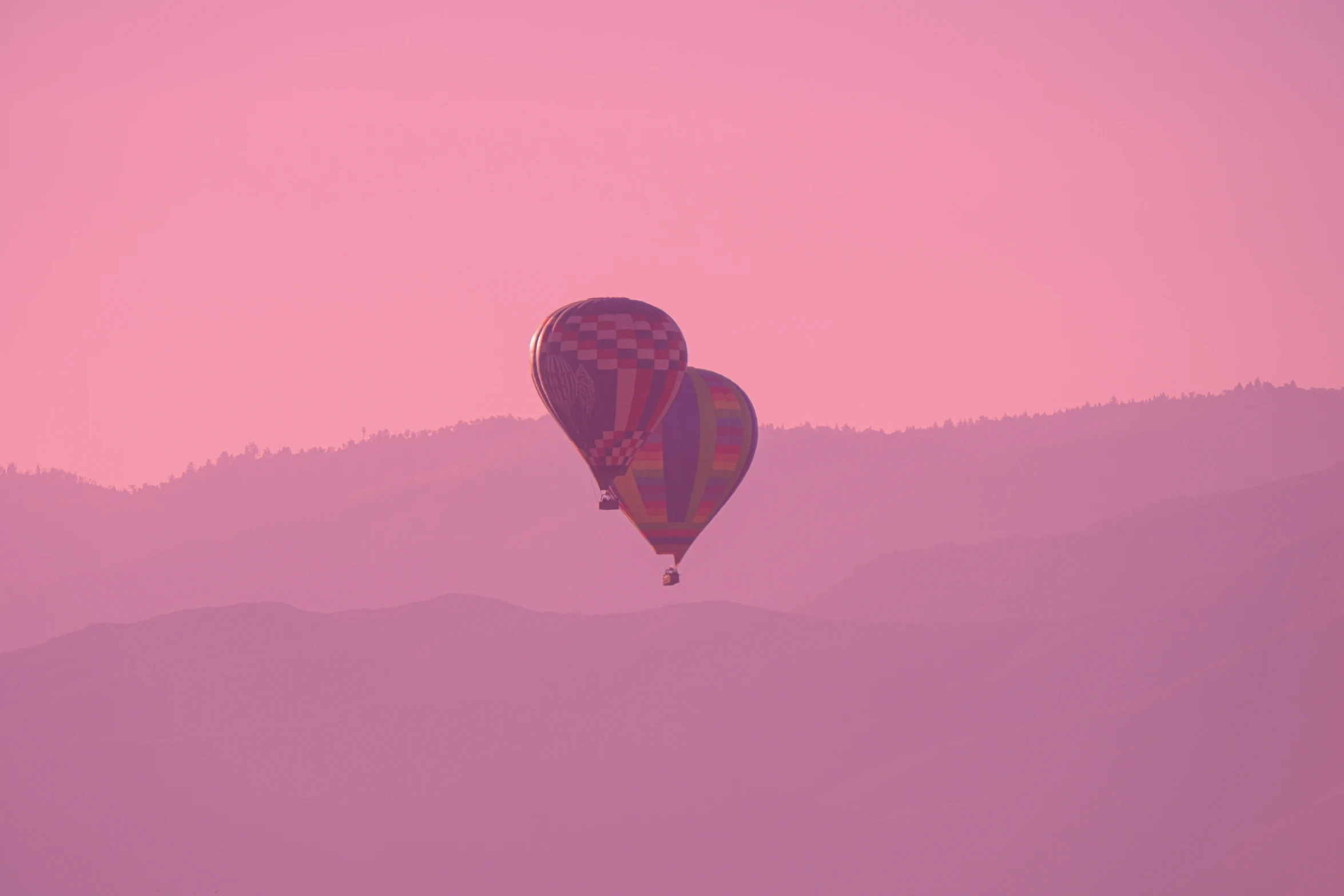 a large and small  air balloon flying over a mountain