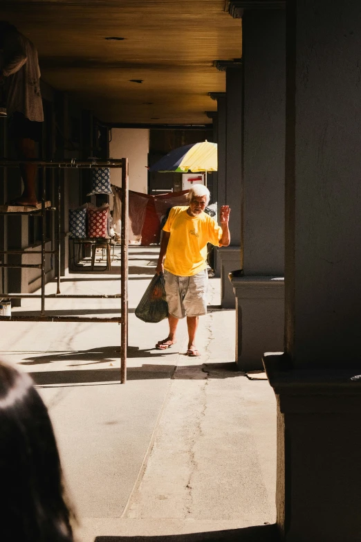 man with yellow umbrella walking on sidewalk underneath covered patio area