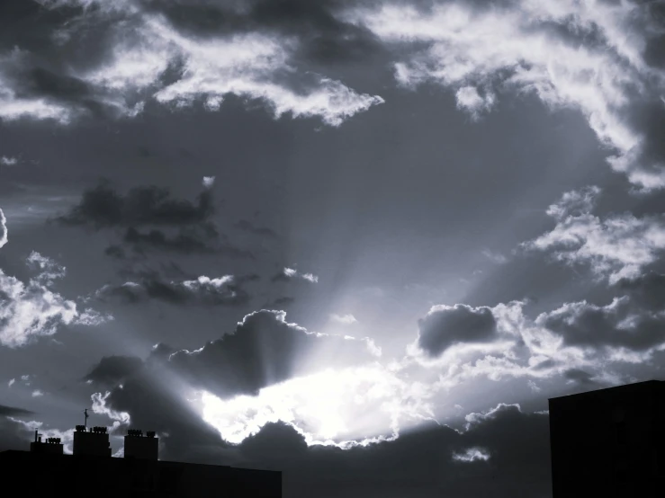 sun rays over dark city skylines with buildings silhouetted against the cloudy sky