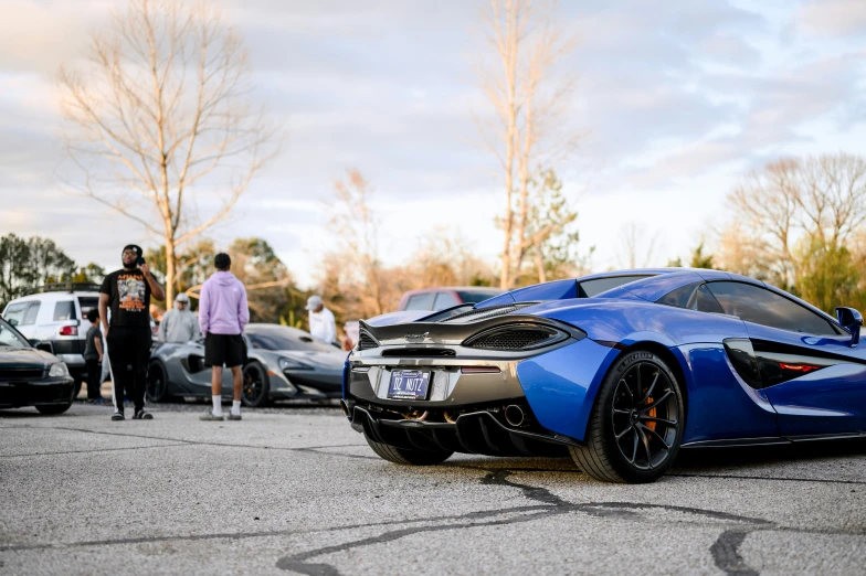 a blue sports car is parked next to a parking lot with people