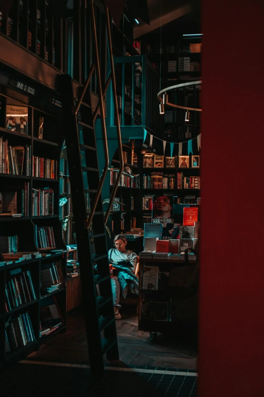 a man sits in the corner of a bookcase next to a ladder