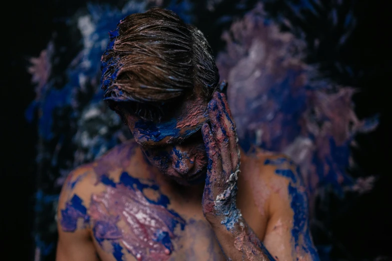 a man covered in paint covering his face with his hands