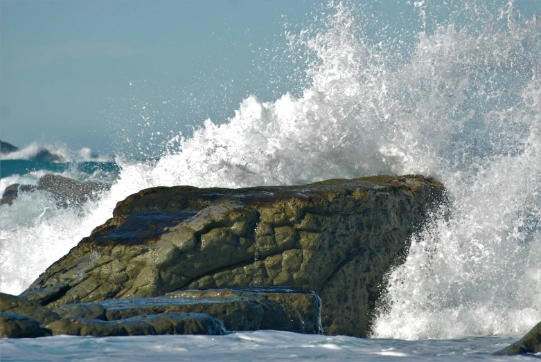 the ocean sprays as it begins to break on top of the rocks