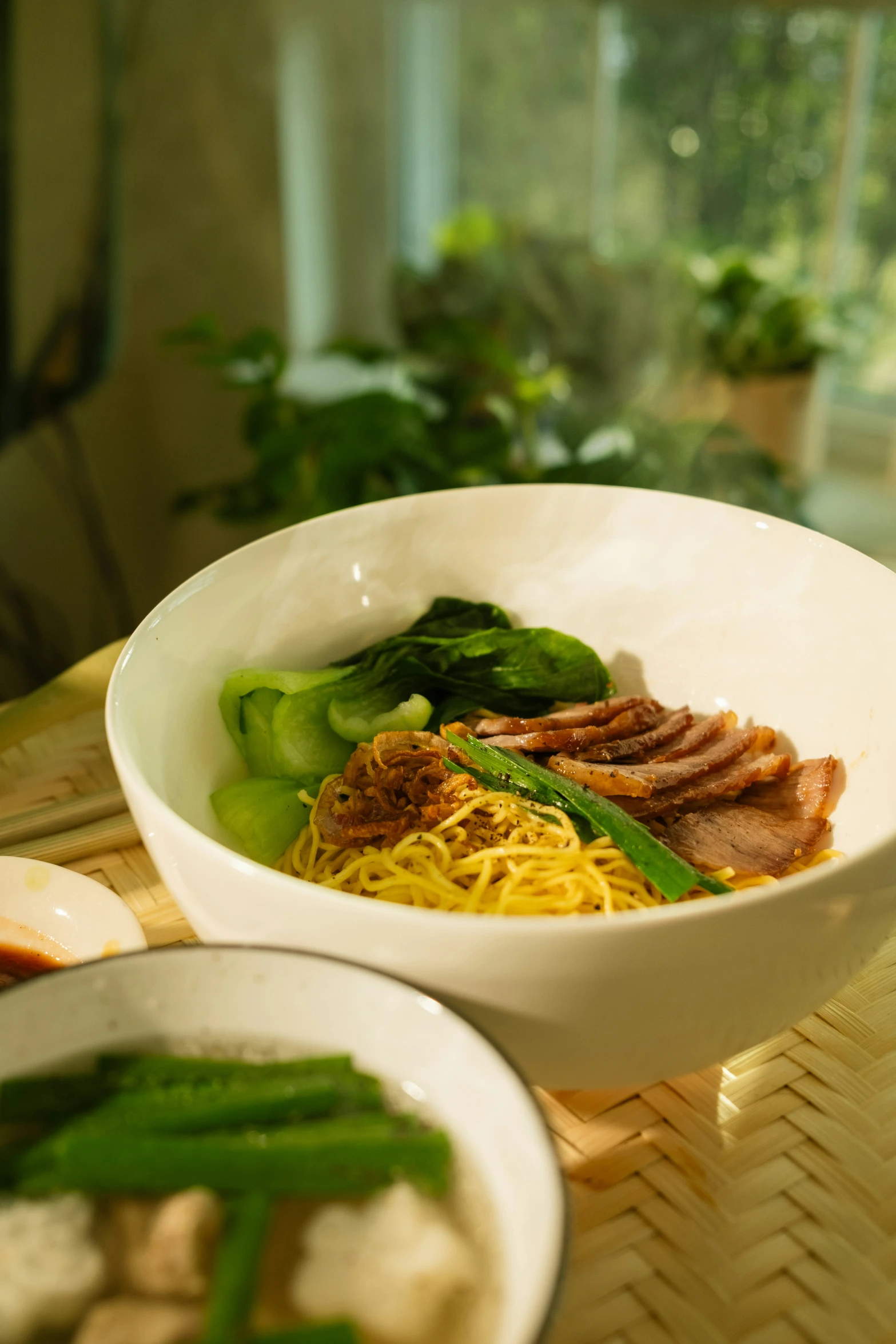 a bowl of noodles and meat is sitting on a table next to a window