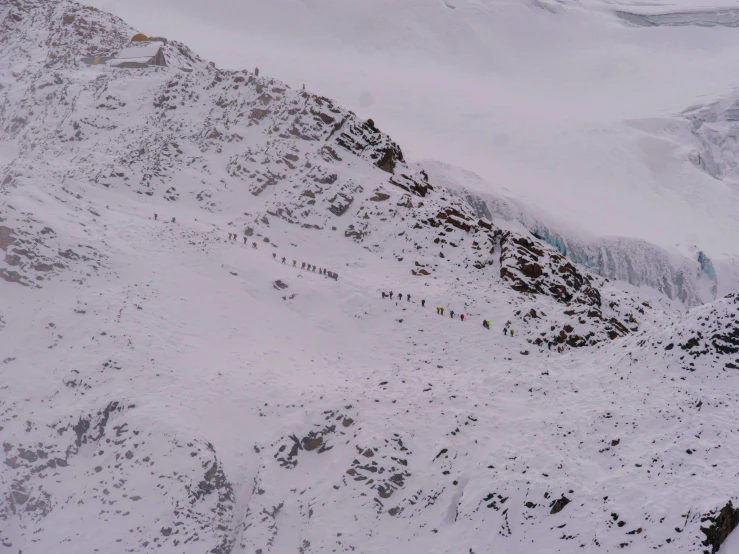 a number of people are walking up the side of a snow covered mountain