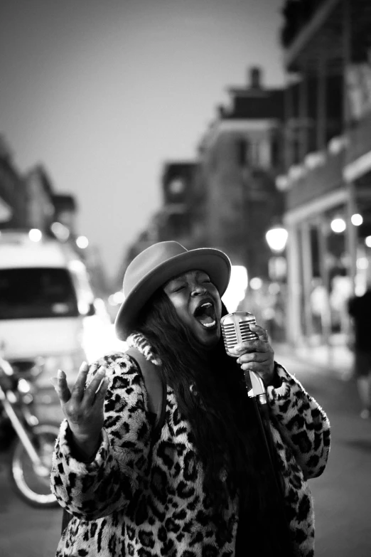 a woman singing into a microphone standing on the side of a road