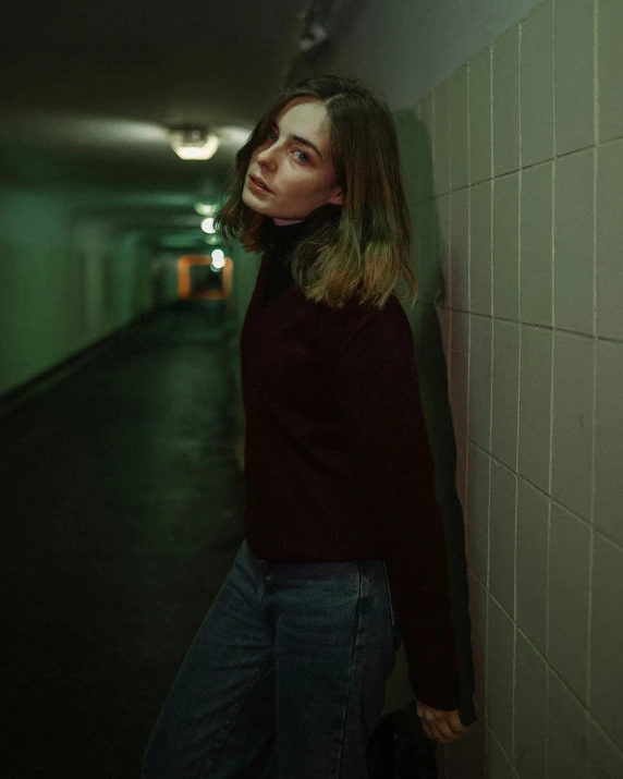 a woman with dark hair and brown sweater standing by a wall