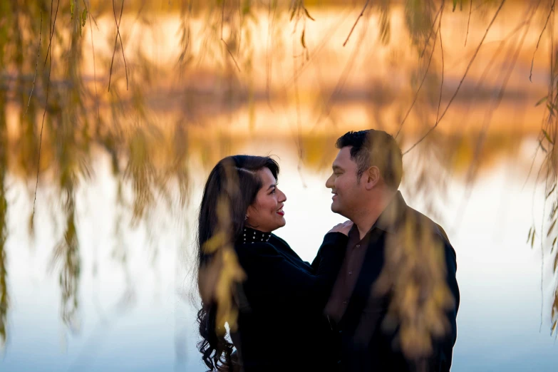 a couple smiling and standing under the tree nches