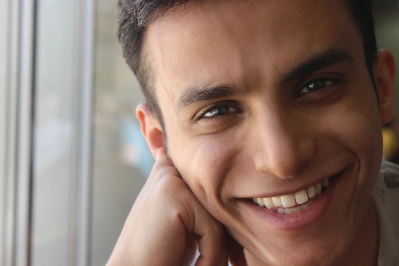 man smiling while he leans with his hands on his chin