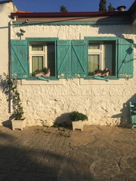 an old white building has blue shutters and a chair on the outside