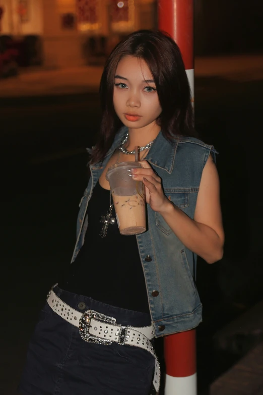 a beautiful young lady standing next to a pole holding a coffee cup