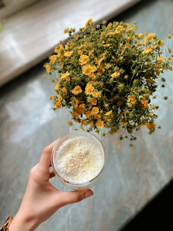 a hand holding a glass with foam and flowers in the background