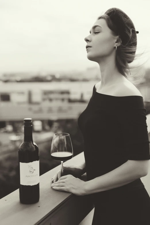 a woman wearing black is looking at the sky, she has a wine bottle and a glass
