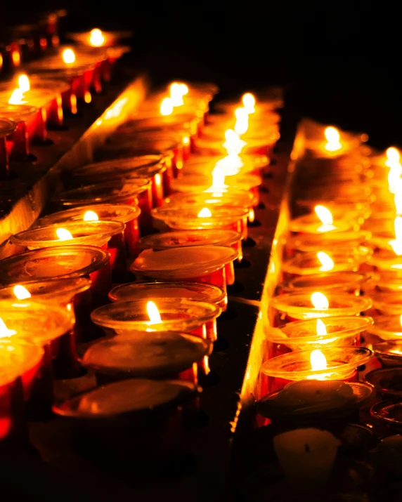 many lit candles are arranged in rows on the floor