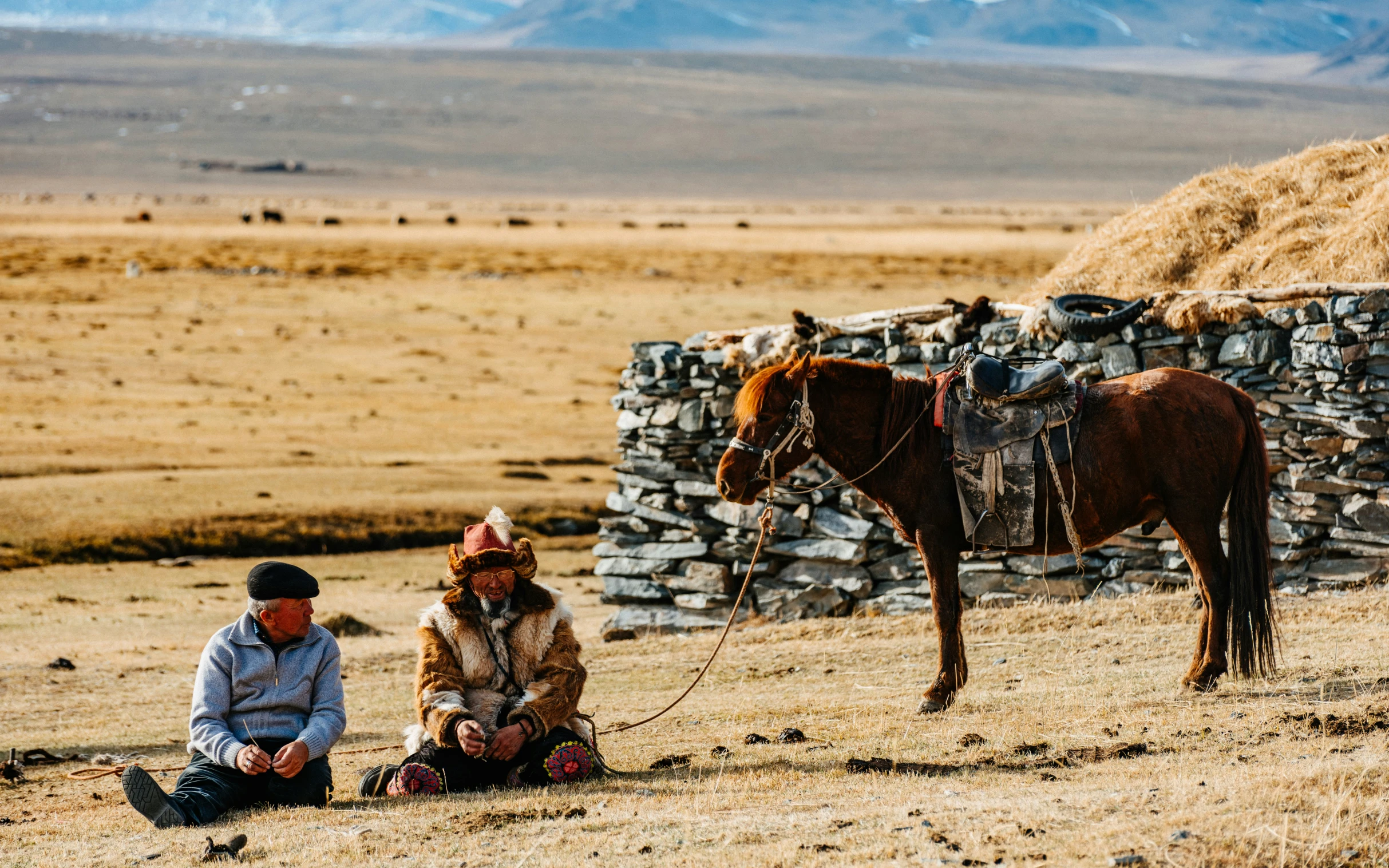 two people are sitting by the ground and one is leaning to the horse