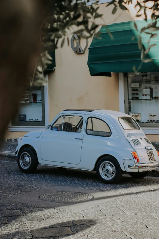 an old white car sits in front of a green awning