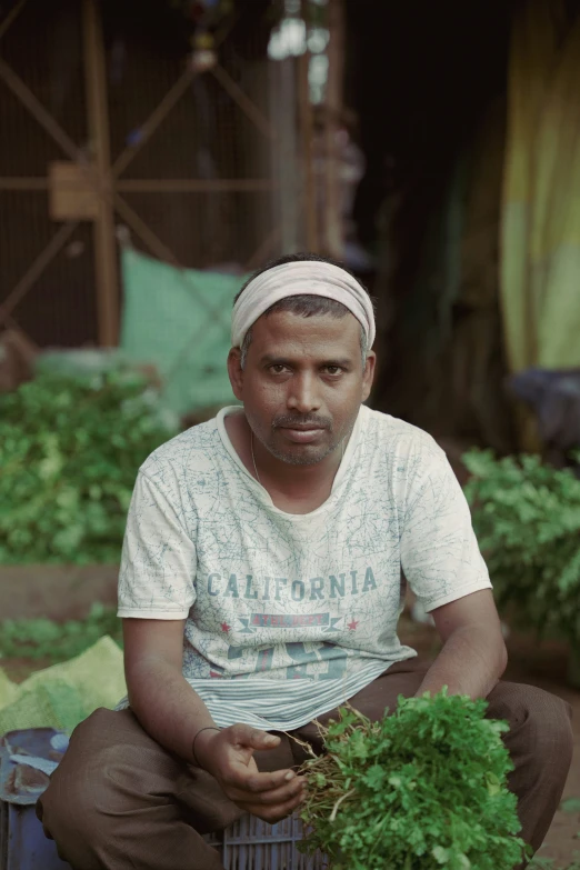 a man wearing a headscarf sitting outside holding plants