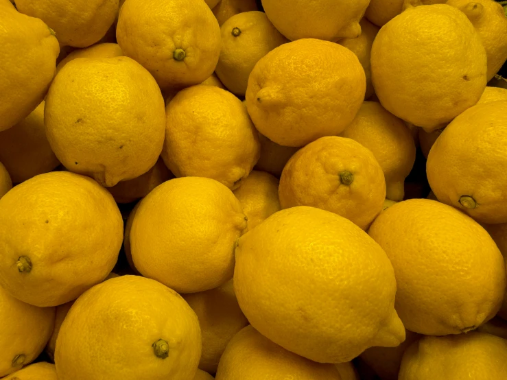 a pile of lemons that are yellow with green tops