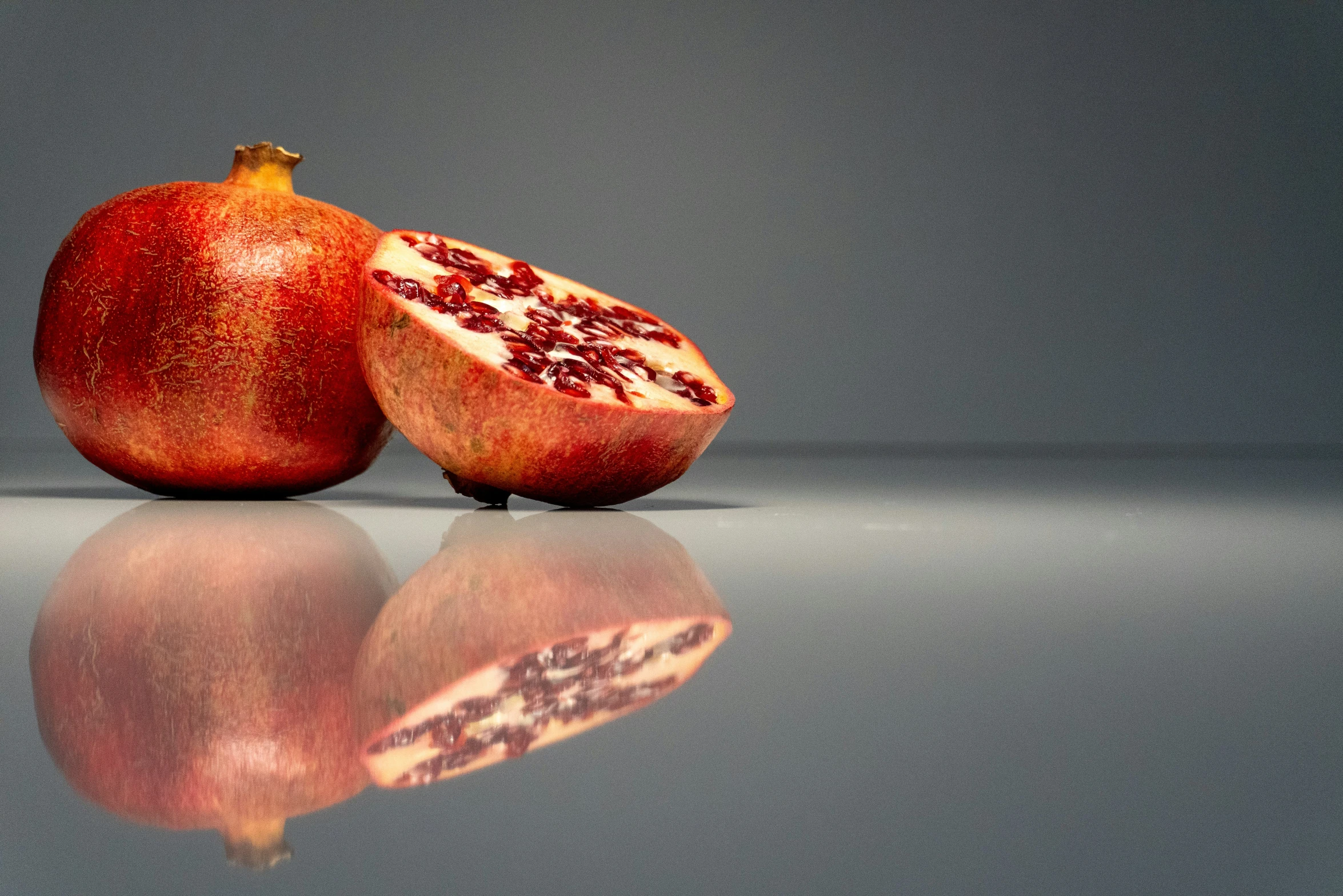 one half of a ripe pomegranate is displayed with its reflection on the ground