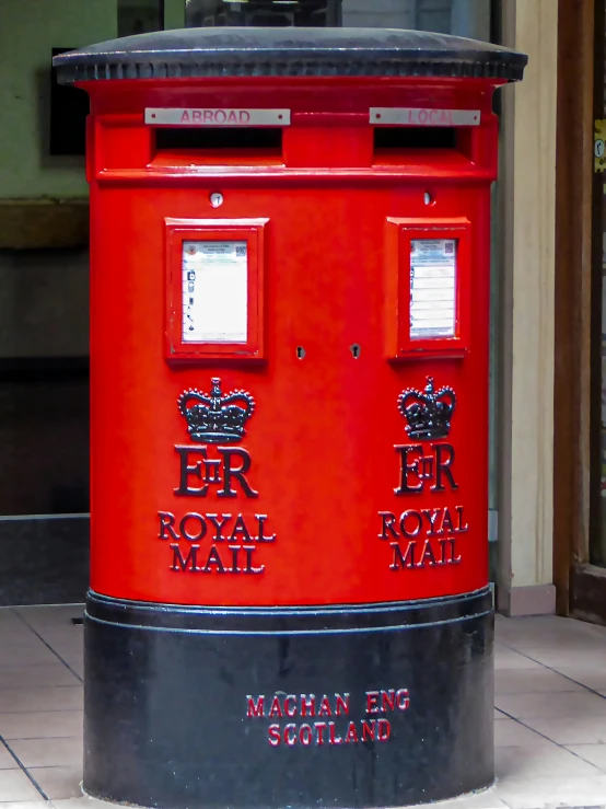 a red post box stands on a tile floor