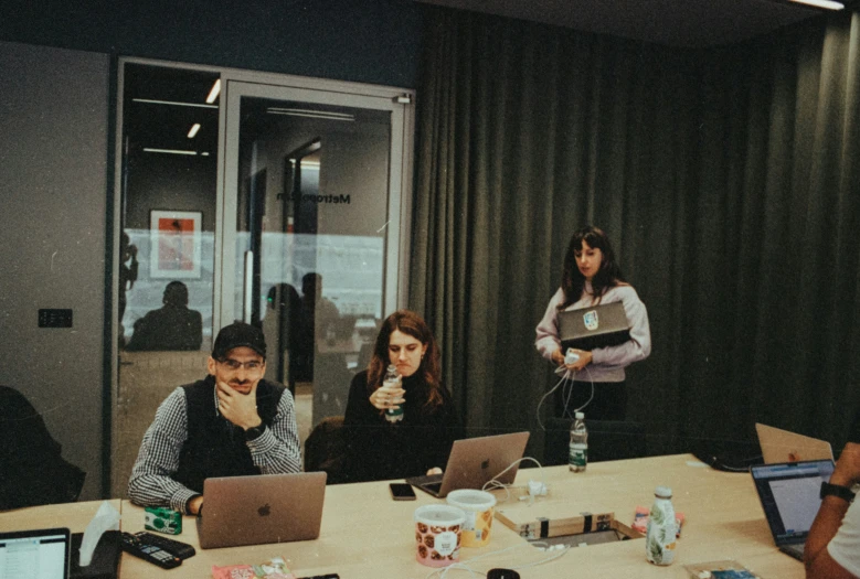 several people sitting around tables with laptops in front of them