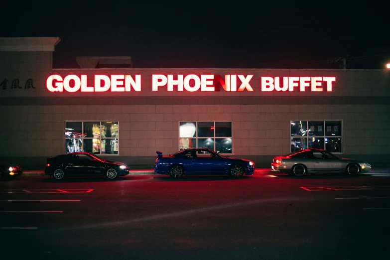 three cars outside a store at night with a light up sign above them